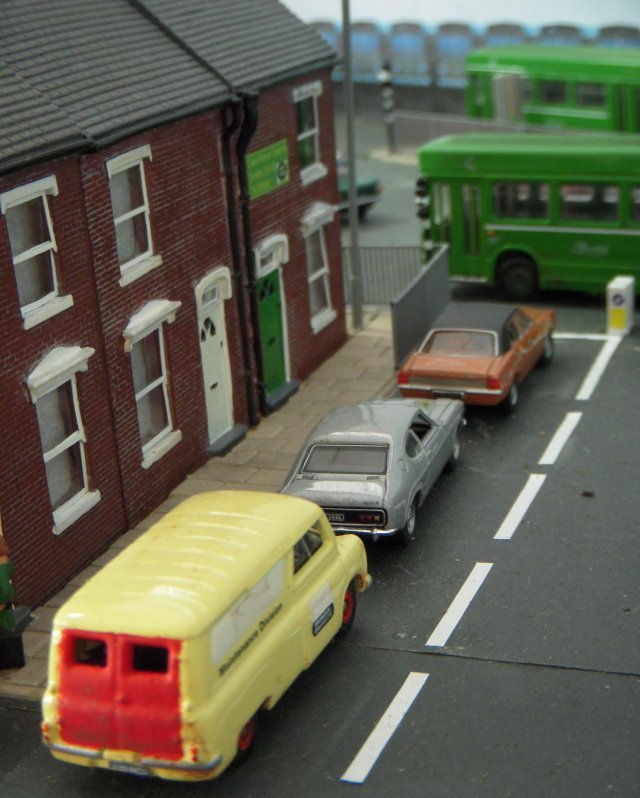 Pallet Lane was an imaginary BR station set around 1977, inspired by the Severn Beach to Bristol branch and built on baseboards recovered from two forklift pallets. The line would have continued beyond Pallet Lane in pre Beeching times but nearby factories and oil and cement terminals ( pictured above) justified its continued survival and that of a DMU passenger service. Already known for his modelling demonstrations at St Margaret's Hall, Rob Owst had made a particularly fine job of the "distressed" scenery at Pallet Lane, especially the corrugated iron platform shelter which was weathered with real rust! The cement terminal was based on that at nearby Lawrence Hill and the fuel oil siding on the 8'6" x 1'6" layout was similar to ones around Shirehampton. However, the location of Pallet Lane can vary with the weathered BR blue stock used and a welcome addition for this show was the town area, including the Land Rover enthusiast's back yard behind the green door on the street pictured below.